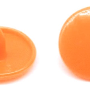 Peut inclure: Quatre boutons-pression en plastique orange, deux avec un centre sur&eacute;lev&eacute; et deux avec un centre plat.