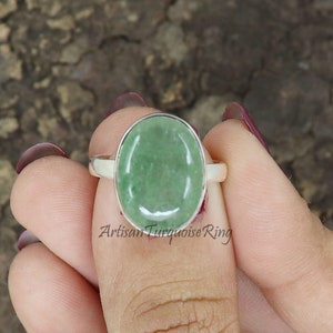 May include: A silver ring with a green oval gemstone. The ring is on a finger.