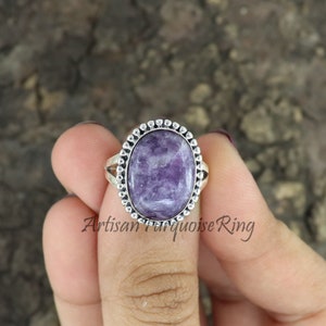 K&ouml;nnte beinhalten: Ein silberner Ring mit einem violetten Edelstein, der in einer Perlenfassung sitzt. Der Ring befindet sich an einem Finger.