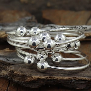 Puede incluir: Un conjunto de anillos apilables de plata con cuentas redondas. Los anillos est&aacute;n superpuestos y las cuentas est&aacute;n dispuestas en un patr&oacute;n aleatorio.