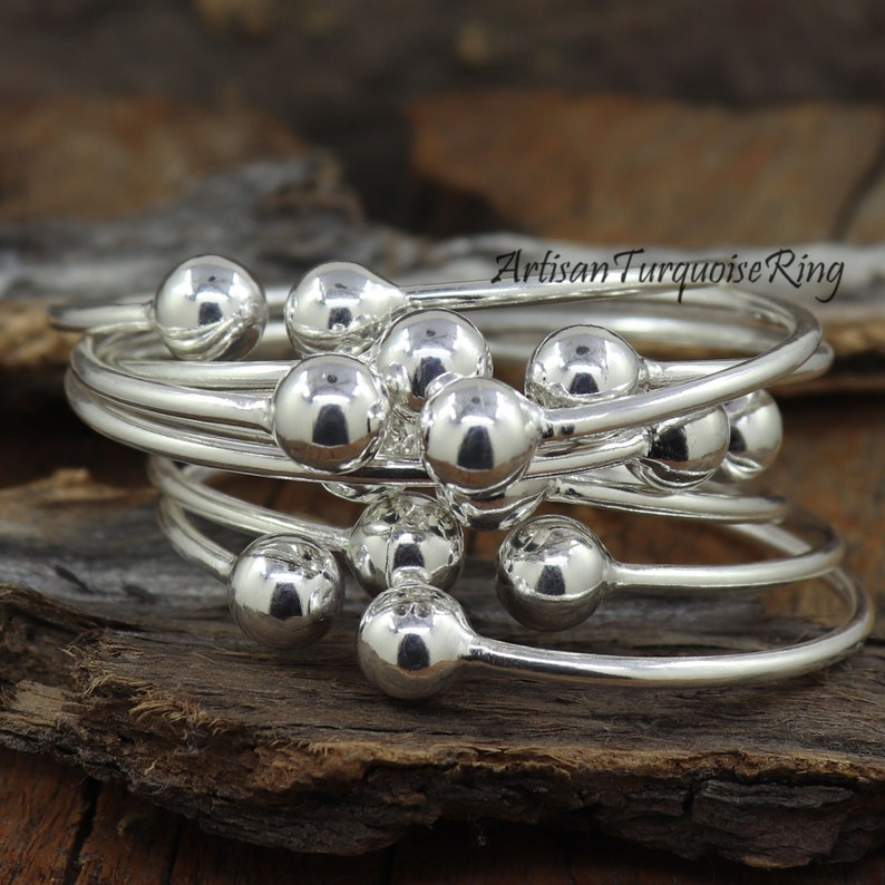 Puede incluir: Un conjunto de anillos apilables de plata con cuentas redondas. Los anillos est&aacute;n superpuestos y las cuentas est&aacute;n dispuestas en un patr&oacute;n aleatorio.
