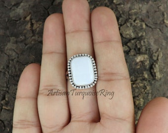 Può includere: Un anello con una pietra bianca e una montatura in argento con perline. L'anello è su un dito.