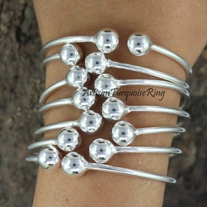 Puede incluir: Un conjunto de pulseras de plata con acentos de bolas redondas. Las pulseras est&aacute;n apiladas una encima de la otra, creando un look en capas.