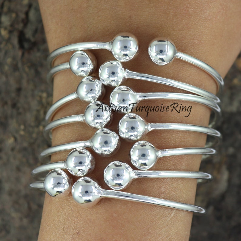 Puede incluir: Un conjunto de pulseras de plata con acentos de bolas redondas. Las pulseras est&aacute;n apiladas una encima de la otra, creando un look en capas.