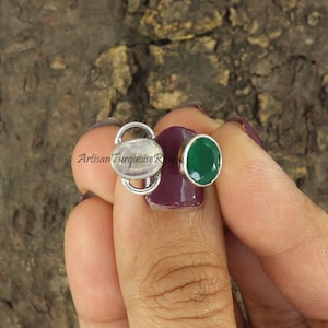 Könnte beinhalten: Ein silberner Ring mit zwei ovalen Edelsteinen. Der größere Stein ist weiß und der kleinere ist grün. Der Ring wird an einem Finger getragen.