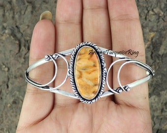 May include: Silver cuff bracelet with a large oval-shaped brown and white stone set in the center. The bracelet has a delicate, intricate design.