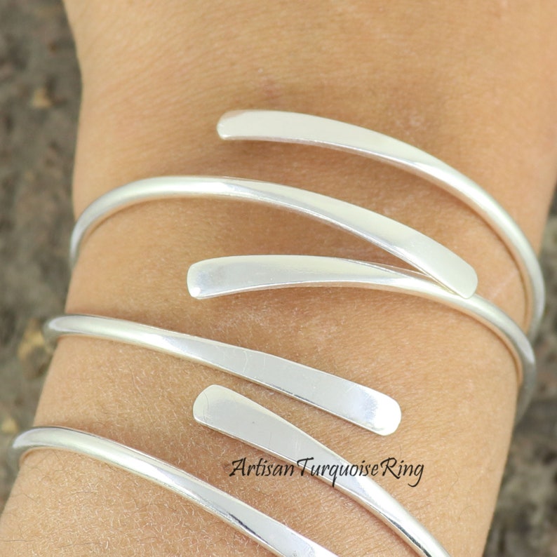 Puede incluir: Pulsera de brazalete de plata con un dise&ntilde;o simple y moderno. La pulsera est&aacute; hecha de m&uacute;ltiples bandas delgadas de plata que se envuelven alrededor de la mu&ntilde;eca. Las bandas son lisas y pulidas, y tienen una forma ligeramente curvada.