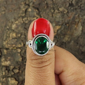May include: A silver ring with a green gemstone set in a circular bezel. The ring has a twisted band and a delicate design.