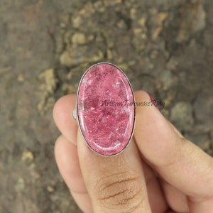 Peut inclure: Une bague en argent avec une grande pierre précieuse ovale rose. La pierre précieuse a un motif moucheté.