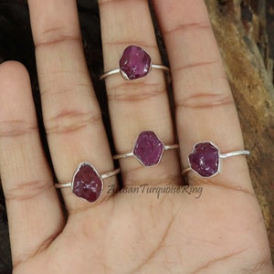 Può includere: Quattro anelli d'argento con pietre preziose di rubino rosa. Gli anelli sono su una mano, con il testo "Artisan Turquoise Ring" visibile nell'immagine.