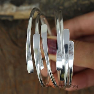 Puede incluir: Un brazalete de plata hecho de m&uacute;ltiples bandas finas y retorcidas. Las bandas son lisas y brillantes, y est&aacute;n dispuestas en un patr&oacute;n de cruz.