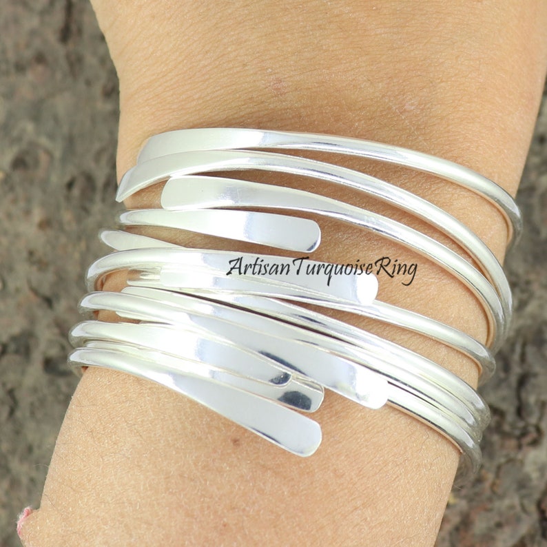 Puede incluir: Un brazalete de plata hecho de m&uacute;ltiples bandas delgadas y superpuestas. El brazalete se lleva en la mu&ntilde;eca.