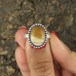 May include: A silver ring with a beaded border and a light brown oval gemstone. The ring is on a finger.