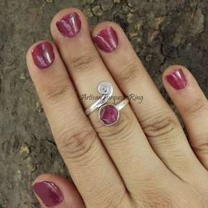 May include: A silver ring with a pink gemstone set in a swirl design. The ring is on a person's finger. "Artisan Turquoise Ring" is written on the image.