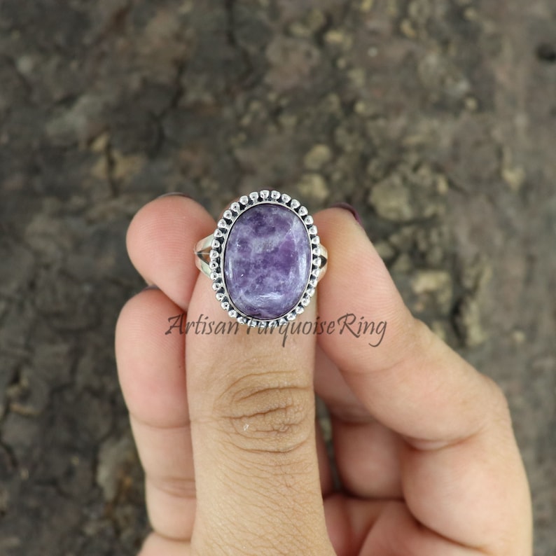 K&ouml;nnte beinhalten: Ein silberner Ring mit einem violetten Edelstein, der in einer Perlenfassung sitzt. Der Ring befindet sich an einem Finger.