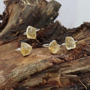 Peut inclure: Quatre bagues en argent avec des pierres de citrine jaune brut. Les bagues sont présentées sur un morceau de bois usé.