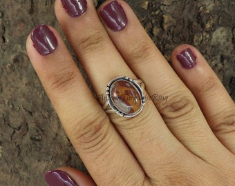 May include: A silver ring with an oval-shaped brown and white stone set in a silver bezel. The ring is on a finger with dark purple nail polish.