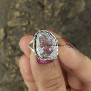 May include: A silver ring featuring a large, clear, faceted gemstone. The ring has a braided band and a textured setting.