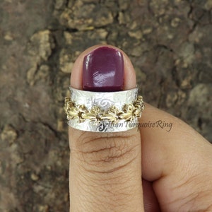 Könnte beinhalten: Ein silberner Daumenring mit einer strukturierten Oberfläche und einem Band aus goldenen Akzenten. Der Ring wird an einem Finger mit burgunderfarbenem Nagellack getragen.