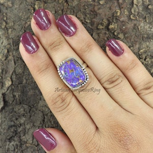 May include: A silver ring with a large, rectangular purple and gold stone set in a silver bezel. The stone has a marbled pattern and is surrounded by a silver rope design.
