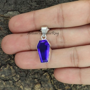 May include: A silver coffin pendant with a purple gemstone. The pendant is on a silver chain.