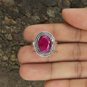 Op de afbeelding: Een zilveren ring met een ovale roze edelsteen gezet in een zilveren bezel met een touwachtig ontwerp. De ring is op een vinger.