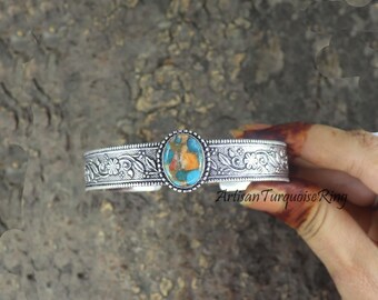 Puede incluir: Brazalete plateado con una piedra ovalada turquesa y naranja. El brazalete presenta intrincados diseños florales y de hojas. El texto "Artisan Turquoise Ring" es visible.