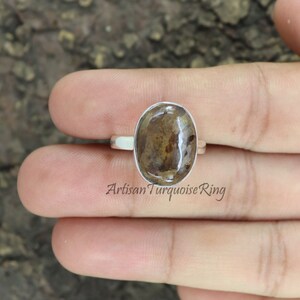 May include: A silver ring with a brown oval gemstone. The gemstone has a unique pattern of brown and white swirls. The ring is set in a simple silver band. Artisan Turquoise Ring.