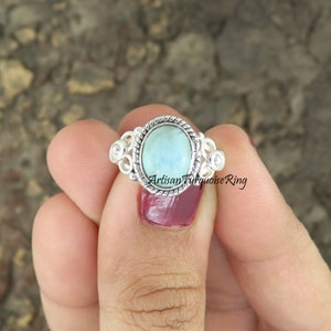 May include: A silver ring with a light blue oval turquoise stone set in a decorative silver bezel. The ring has a delicate, intricate design with small silver accents.