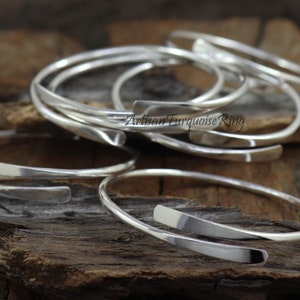 Puede incluir: Un conjunto de pulseras de plata con una banda plana y ancha. Las pulseras est&aacute;n apiladas unas sobre otras, y el texto "Artisan Turquoise Ring" es visible en una de las pulseras.