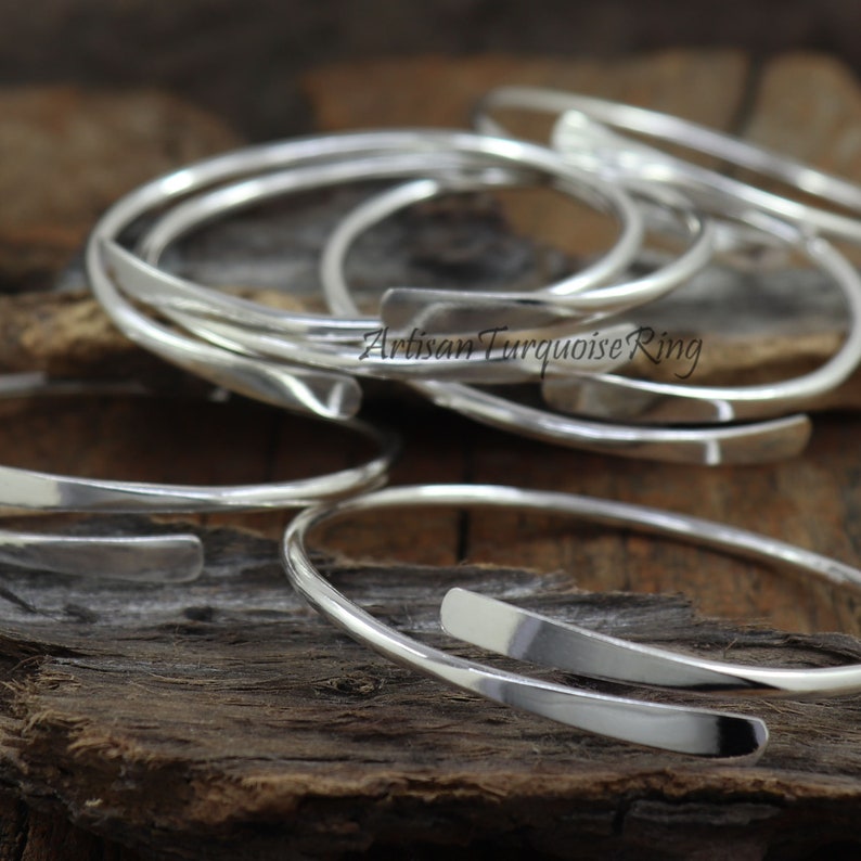 Puede incluir: Un conjunto de pulseras de plata con una banda plana y ancha. Las pulseras est&aacute;n apiladas unas sobre otras, y el texto "Artisan Turquoise Ring" es visible en una de las pulseras.