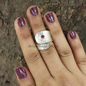 Może przedstawiać: Srebrny pierścionek z fakturowanym wzorem i czerwonym kamieniem szlachetnym. Pierścionek jest owinięty wokół palca i ma młotkowane wykończenie. Artisan Turquoise Ring.