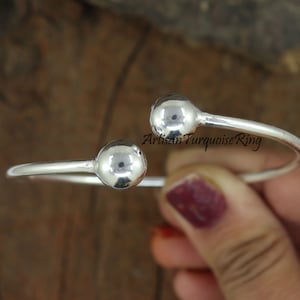 Puede incluir: Pulsera de brazalete de plata con dos bolas redondas en los extremos. La pulsera est&aacute; abierta y se puede ajustar para adaptarse a diferentes tama&ntilde;os de mu&ntilde;eca.