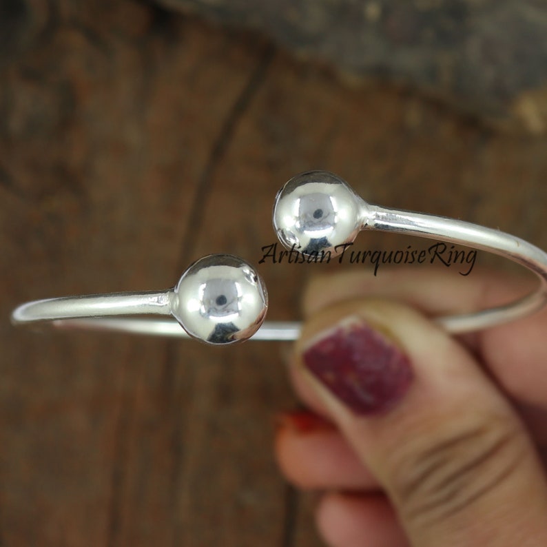 Puede incluir: Pulsera de brazalete de plata con dos bolas redondas en los extremos. La pulsera est&aacute; abierta y se puede ajustar para adaptarse a diferentes tama&ntilde;os de mu&ntilde;eca.