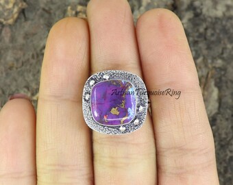 Puede incluir: Un anillo de plata con una piedra cuadrada de color púrpura y dorado engastada en un engaste de plata texturizado. El anillo está en un dedo.