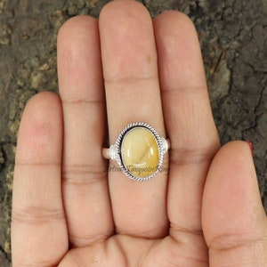 May include: A silver ring featuring a yellow oval gemstone set in a twisted wire bezel. The ring is on a hand, and the text "Artisan Turquoise Ring" is visible below the ring.