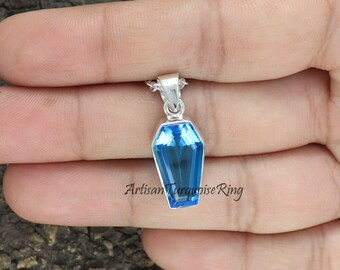 May include: A silver pendant with a blue topaz gemstone in the shape of a coffin. The pendant is hanging from a silver chain.