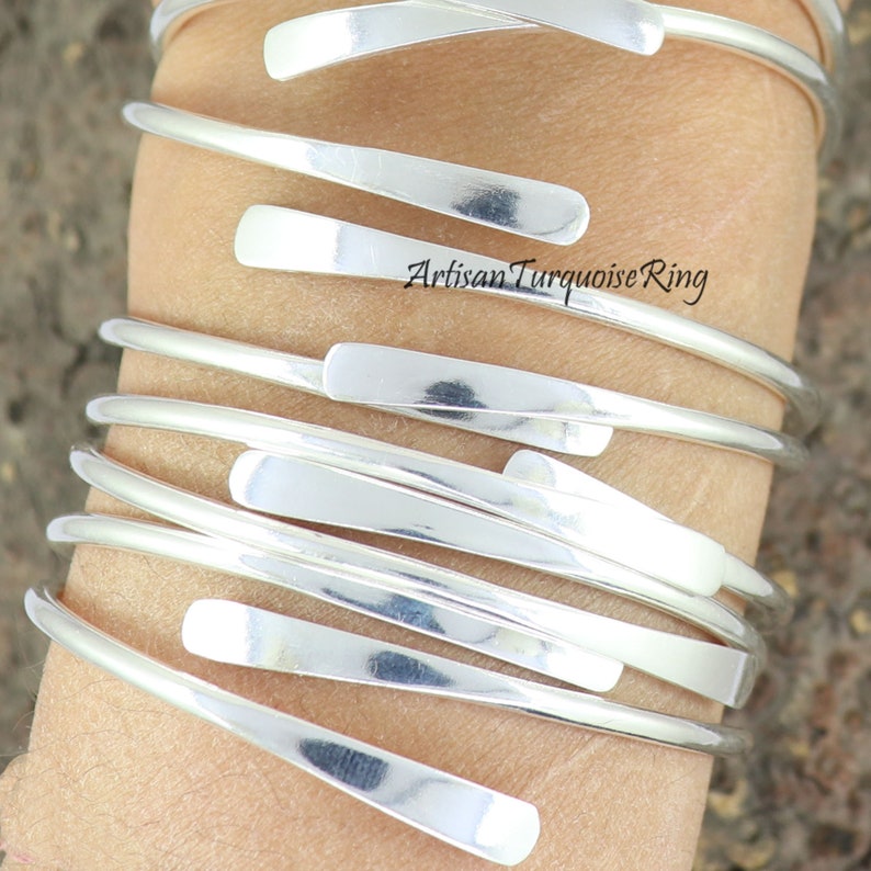 Puede incluir: Un conjunto de pulseras de plata con un dise&ntilde;o plano y rectangular. Las pulseras est&aacute;n apiladas en la mu&ntilde;eca de una persona.