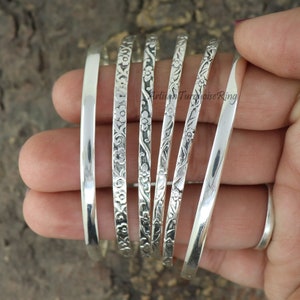 Könnte beinhalten: Sechs silberne Armreifen, einige mit Blumenmustern, auf einer Hand gestapelt. Artisan Turquoise Ring.