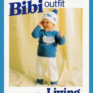 Puede incluir: Un suéter azul tejido con un diseño de pájaro blanco, un gorro blanco tejido con un diseño de pájaro azul y pantalones blancos. La imagen es de una revista de tejido llamada "Living".