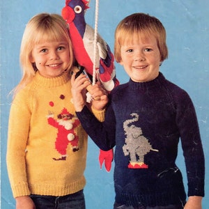 May include: Two children wearing knitted sweaters with colorful designs. The girl is wearing a yellow sweater with a clown design and the boy is wearing a blue sweater with an elephant design. The sweaters are from a Patons Clansman D.K. knitting pattern.
