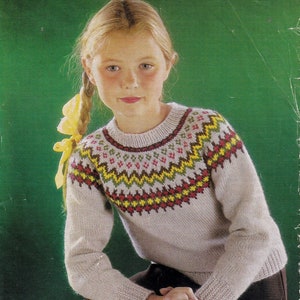 May include: A young girl wearing a beige sweater with a colorful Fair Isle pattern around the neck. The sweater is knitted and has long sleeves. The girl has blonde hair and is wearing black pants. The image is from a knitting pattern book and includes the text "Wendy", "Double Knittings... 26"/28" Chest", "7p 613".