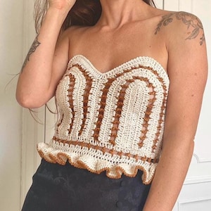 Puede incluir: Top de ganchillo crema y marrón con escote corazón y bajo con volantes. El top presenta un patrón arqueado repetido en marrón, creando un diseño texturizado y detallado. Prenda hecha a mano, ideal para el verano.