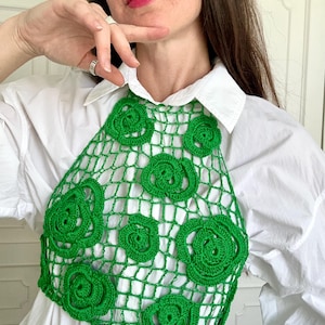 Puede incluir: Un top halter de ganchillo en color verde brillante con una estructura de malla similar a una red, adornado con múltiples motivos florales en espiral en relieve. La prenda es sin mangas y está diseñada para llevarse sobre otra ropa.