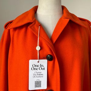 May include: Bright orange coat with a classic collar and black buttons. The coat features a tag that reads "One In, One Out, Change The Future Of Fashion!"