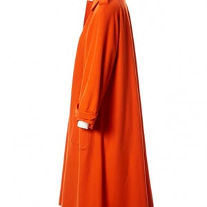 May include: A vibrant orange coat with a classic design. The coat features a collared neckline, long sleeves, and a knee-length hem. The coat is displayed on a mannequin, showcasing its tailored fit and overall style. The coat has a button closure and pockets.
