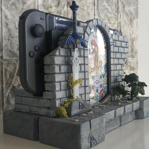 May include: A gray stone-like stand with a gray Nintendo Switch console, a blue sword, and a stained glass window with a colorful design. The stand is designed to look like a castle or a doorway.
