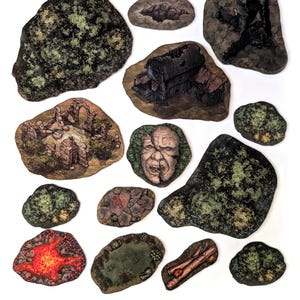 May include: A collection of fantasy terrain pieces, including a dilapidated building, a fiery lava pit, and various rock formations with trees. The pieces are painted with detailed textures and colors, suitable for tabletop gaming or dioramas.