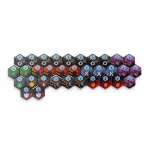 May include: A collection of hexagonal game tiles arranged in a cluster. The tiles feature various colors including black, red, blue, green, and purple, with printed icons such as gears, flames, numbers, and symbols like X, plus signs, and wrenches.