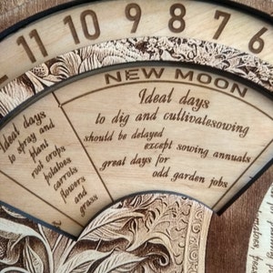 Peut inclure: Un tableau circulaire en bois avec les chiffres 6 &agrave; 11 autour du bord. Le tableau est divis&eacute; en sections avec du texte sur le jardinage et les phases de la lune. Le texte indique "Nouvelle Lune", "Jours id&eacute;aux pour creuser et cultiver les semis doivent &ecirc;tre retard&eacute;s sauf pour les semis annuels", et "Bons jours pour les travaux de jardinage impairs".